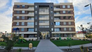 A multi-story residential building with a central entrance, balconies, and a small playground area.