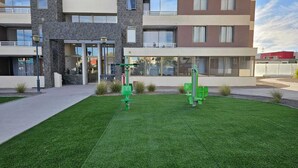 A modern building with a stone facade, large windows, and a well-maintained lawn with exercise equipment.