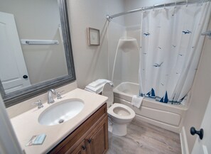 A bathroom with a sink, mirror, toilet, and bathtub.