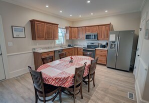 A modern kitchen with wooden cabinets, a granite countertop, a stainless steel refrigerator, and a dining table with chairs.