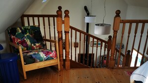 Um quarto com escada de madeira, tapete branco e fofo, e uma cadeira colorida.