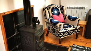 Uma sala de estar acolhedora com uma lareira a lenha preta, uma poltrona estampada, uma cesta de vime e um tapete preto e branco.