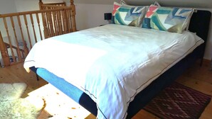Quarto com estrutura de cama de madeira, colcha branca e almofadas coloridas.