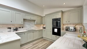 Una cocina moderna con armarios verde claro, encimera de mármol y suelo de madera.