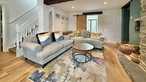 Una sala de estar con chimenea de ladrillo blanco, una escalera de madera y un ventanal grande.