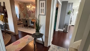 Un amplio salón con suelo de madera, una araña y una mesa de comedor.