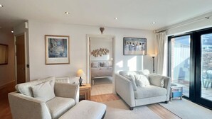 A modern living room with two sofas, a coffee table, and a side table with a lamp. There are framed artworks on the walls and a view of the outside through large windows. - Central Spacious Ground Floor Flat with Courtyard (Kingsbridge)