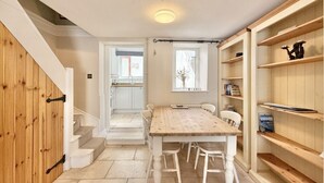 A dining area with a wooden table and chairs, a staircase, and a bookshelf. - Farthing Cottage…cute ‘n’ cosy! (Kingsbridge)