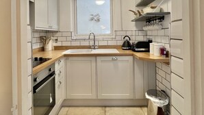 A compact kitchen with white cabinets, a wooden countertop, a window with a view, and a small trash bin. - Farthing Cottage…cute ‘n’ cosy! (Kingsbridge)