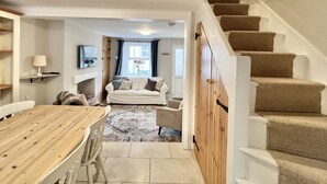 A cozy living room with a sofa, a dining table, and a staircase. - Farthing Cottage…cute ‘n’ cosy! (Kingsbridge)