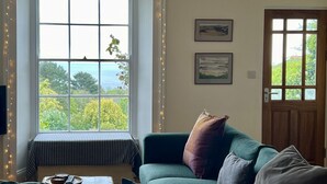 A cozy living room with a green sofa, a bench by a large window overlooking greenery, and string lights.