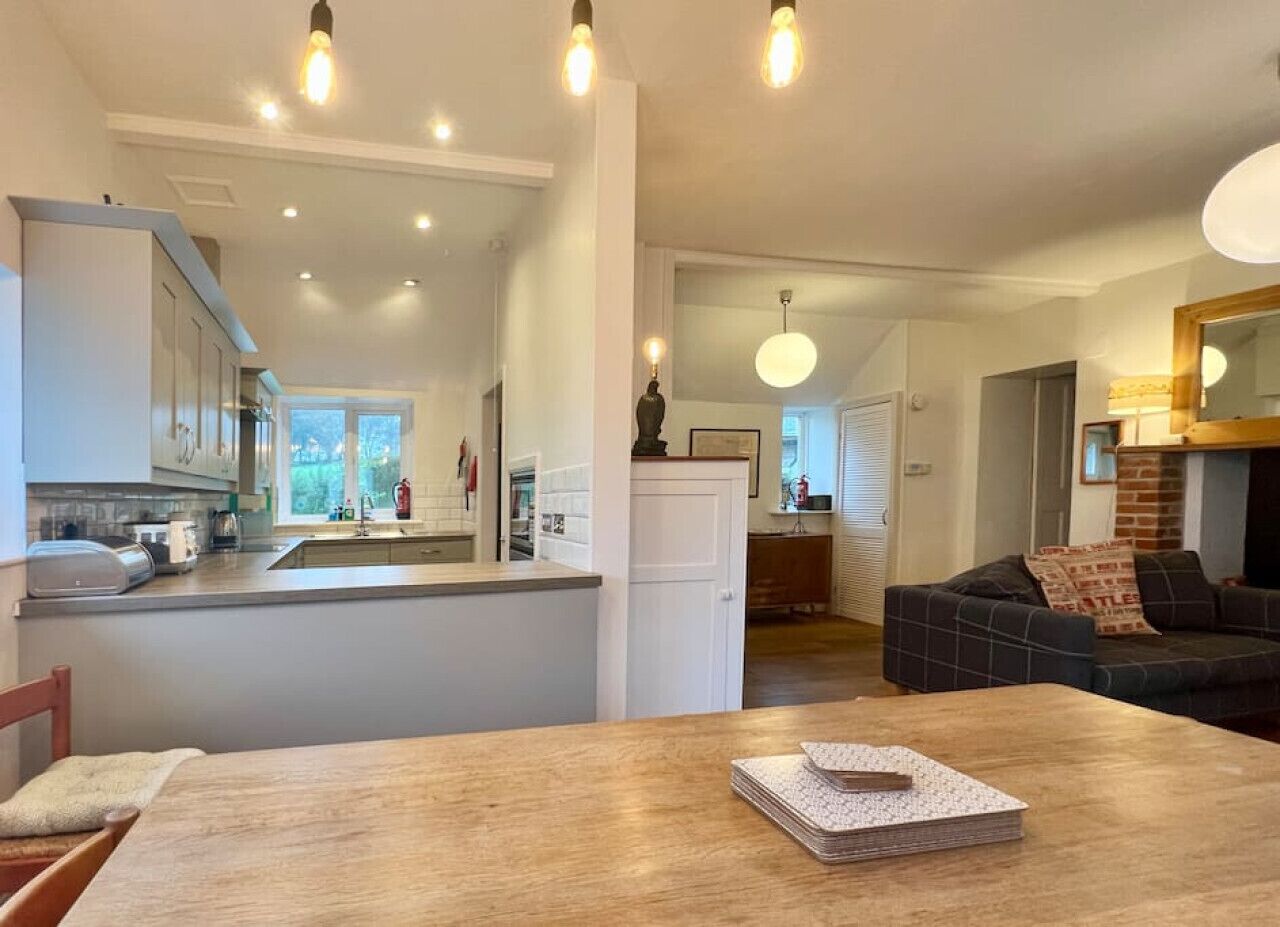 Una cocina moderna con una isla central, un comedor con mesa de madera y una sala de estar con sofá y chimenea.