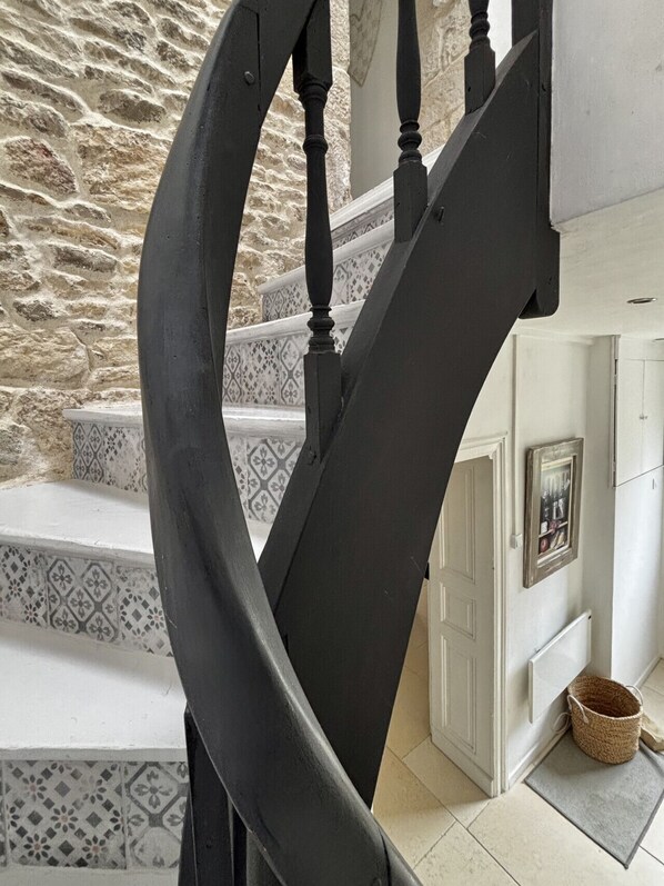 A staircase with a black handrail and patterned steps, leading to a room with a door and a basket on the floor.
