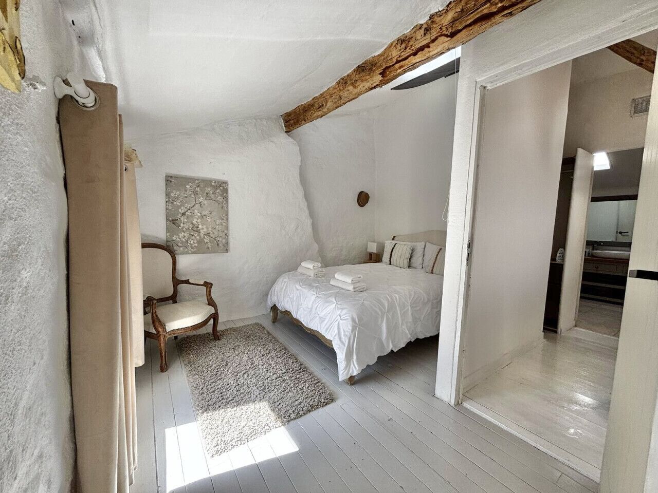 A bedroom with a bed, a chair, a rug, and a painting on the wall.