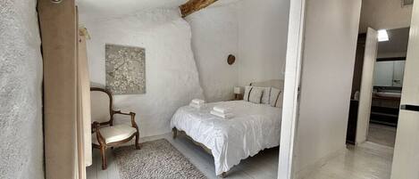 A bedroom with a bed, a chair, a rug, and a painting on the wall.