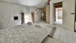 Une chambre à coucher avec un grand lit, une poutre en bois au plafond, un mur en pierre et une porte donnant sur une autre pièce.