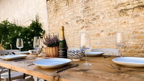 Une table en bois, dressée pour le dîner, avec des assiettes, des verres et une bouteille de vin, le tout mis en valeur par un mur de pierres en arrière-plan.