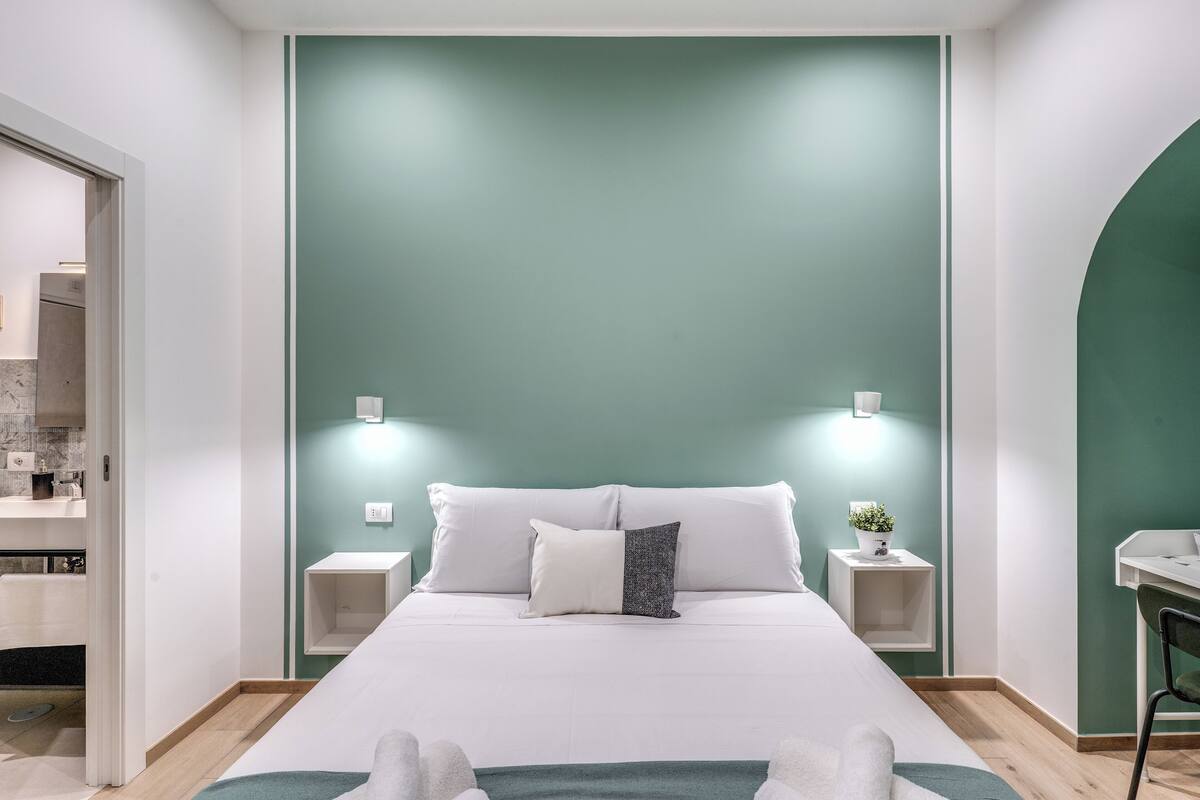 A modern bedroom with a large bed, two bedside tables, a nightstand, and a green accent wall.