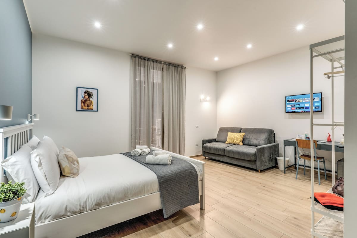 A modern bedroom with a bed, a grey sofa, a desk, and a TV.