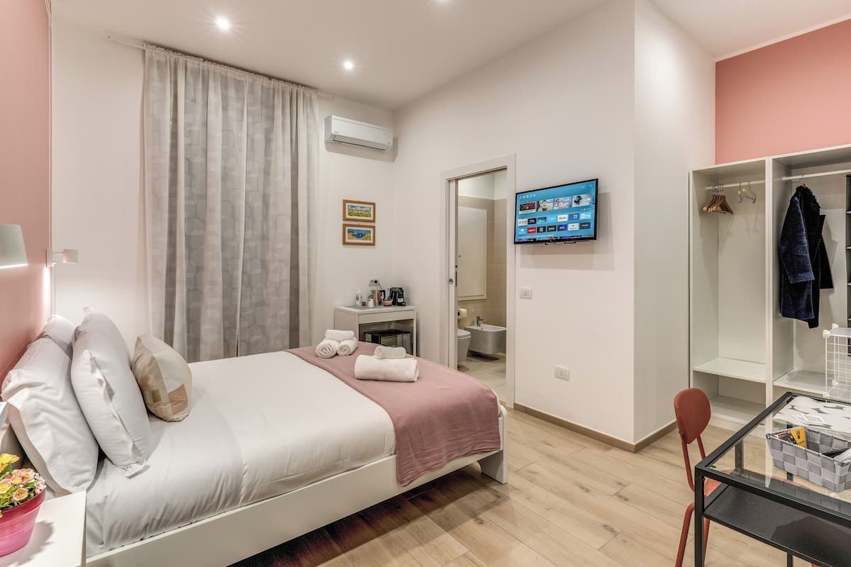 A modern bedroom with a bed, a desk, a chair, a TV, and a wardrobe.