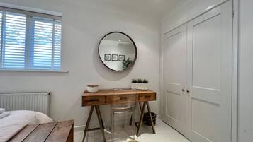 A bedroom with a wooden desk, a round mirror, a white radiator, a window with blinds, and a white door.