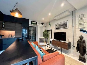 Una sala de estar moderna con área de cocina, un sofá, un televisor y una estatua.