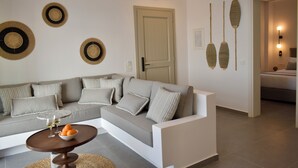 A modern living room with a grey sofa, a round coffee table with oranges and glasses, and wall decor including circular and leaf-shaped patterns.