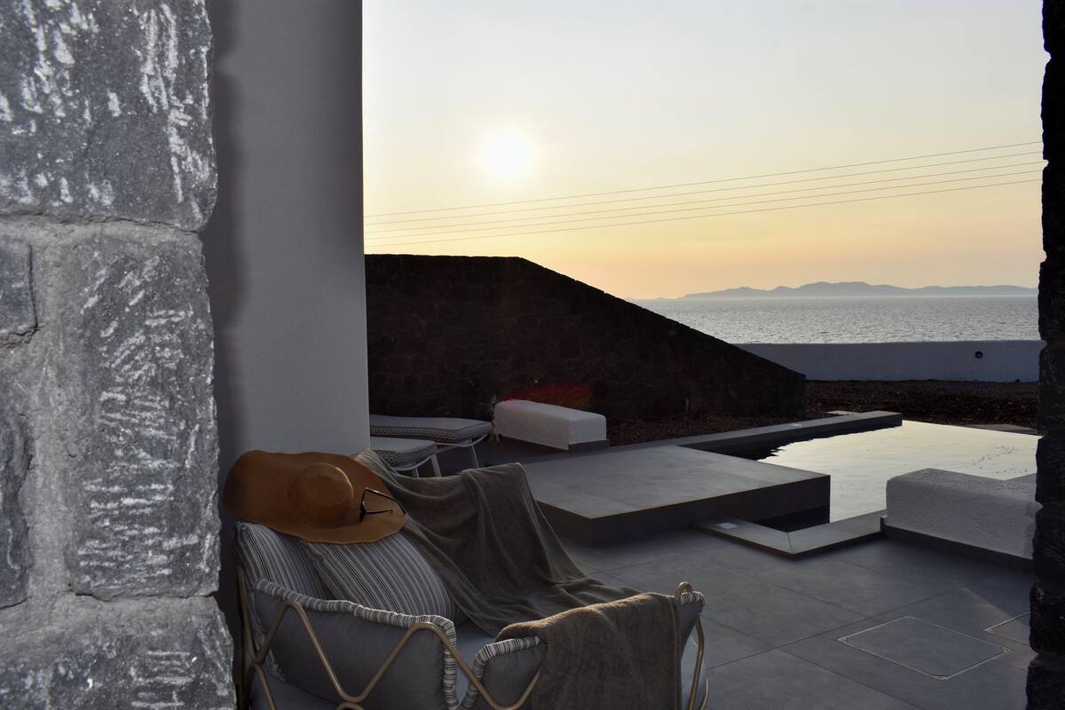 A modern outdoor seating area with a view of the sea at sunset.