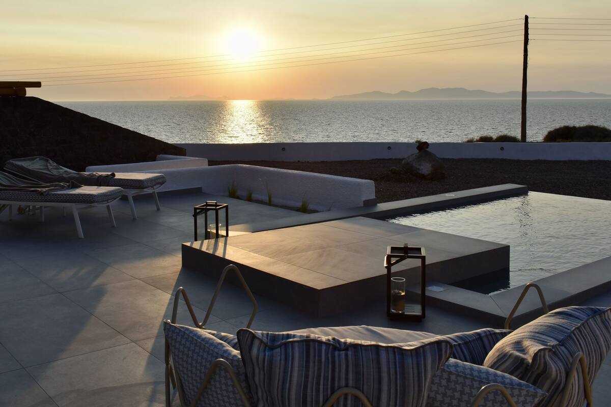 A rooftop terrace with a pool, lounge chairs, and a view of the sunset over the sea.