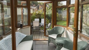 Een oranjerie met rieten meubilair, een glazen deur en uitzicht op een tuin.