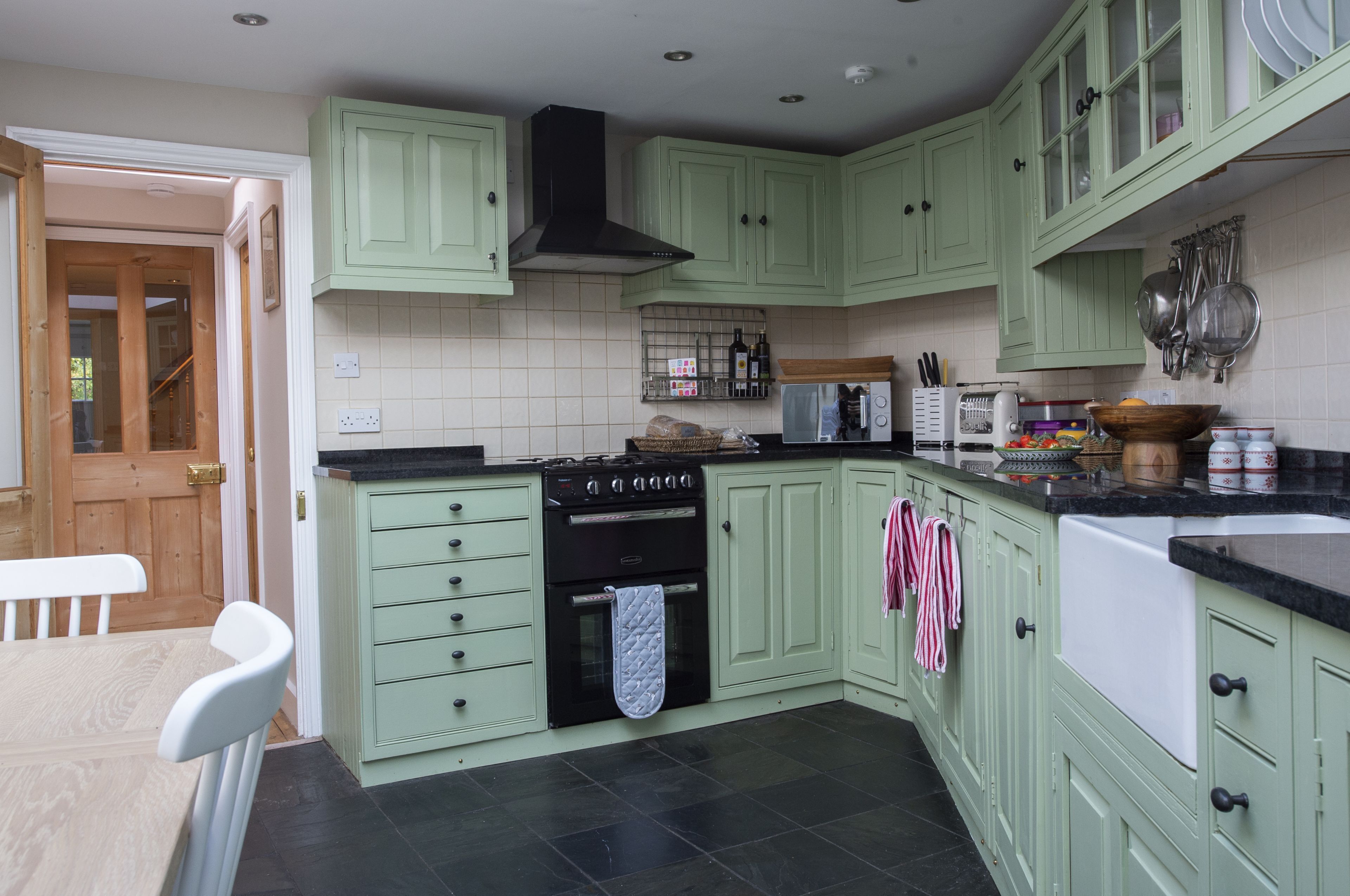 A kitchen with green cabinets, a stove, oven, microwave, and various kitchen utensils.