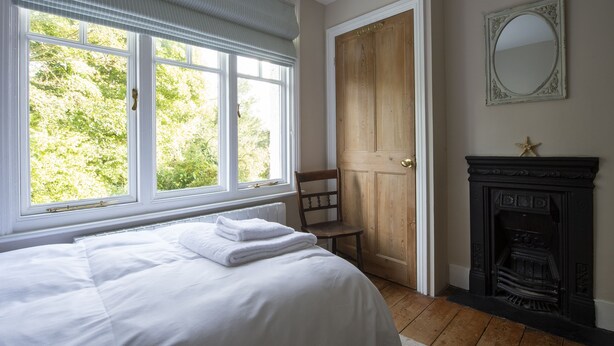 Een slaapkamer met een groot raam, een houten deur, een open haard en een spiegel aan de muur.