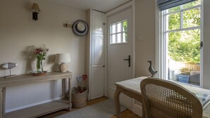 Een kamer met een houten console tafel, een rieten stoel, een witte deur en een raam met uitzicht op groen.