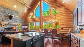 A spacious log cabin with a stone fireplace, a large kitchen with a stove, and a dining area with a view of the outdoors.