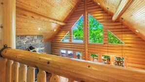 A wooden interior with a stone fireplace, wooden beams, and a wooden railing.