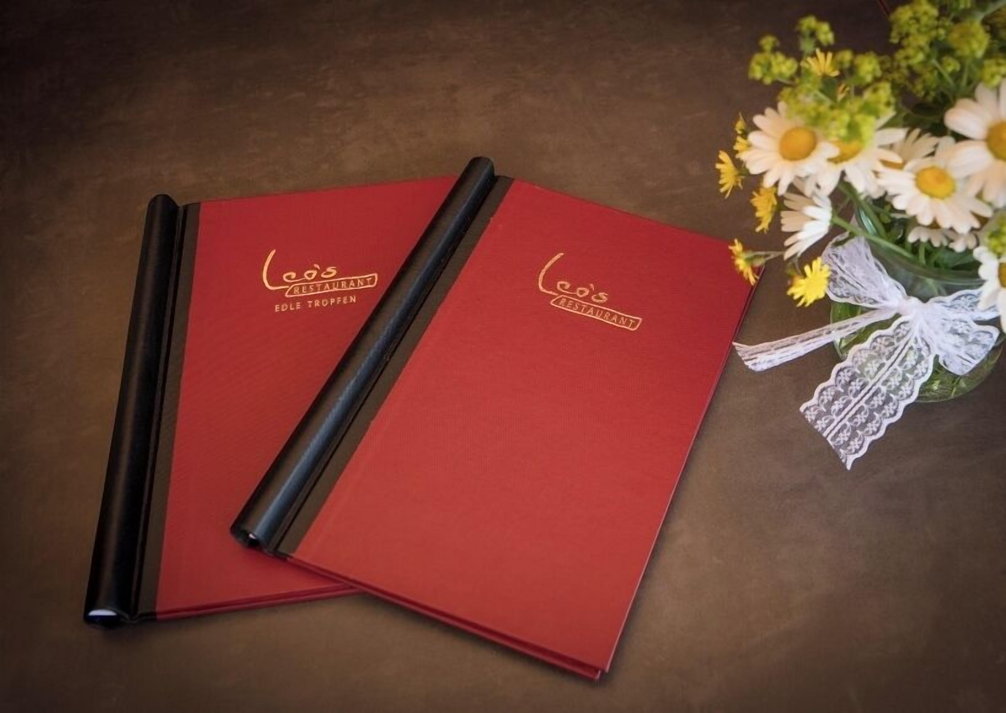 Two red folders with 'Leo's Restaurant' logo on a brown surface.