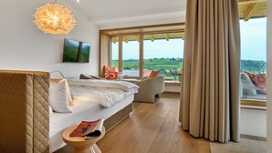 A modern bedroom with a large window, a bed, a sofa, and a hanging light fixture. - Anetseder Landhotel & Lofts (Thyrnau)