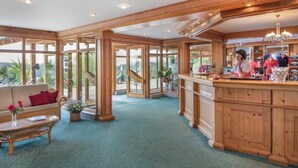 A hotel lobby with a wooden interior, a reception desk, and large windows offering a view of the outdoors. - Anetseder Landhotel & Lofts (Thyrnau)