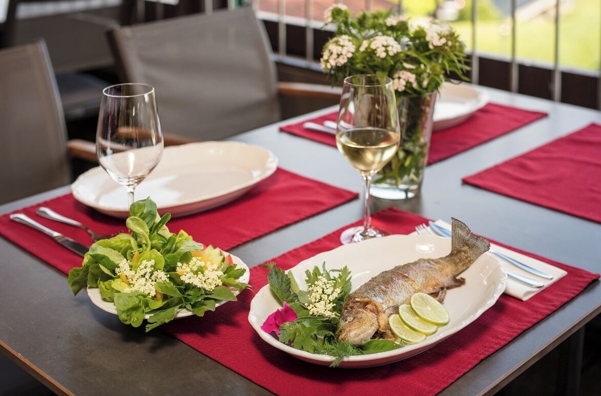 A dining table set with plates of fish, a glass of white wine, and a vase of flowers.