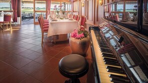 A dining area with a piano, a large flower vase, and a view of the outdoors. - Anetseder Landhotel & Lofts (Thyrnau)