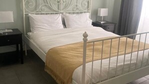 A neatly made bed with white bedding and a beige throw blanket, a white metal headboard, and a bedside table with a lamp. - La Terrazza su Palermo : Camera Matrimoniale Deluxe con Vasca (Palermo)