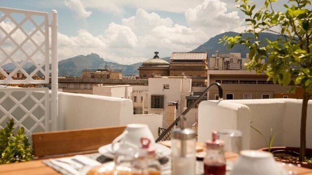 A rooftop terrace with a table set for breakfast, overlooking a cityscape and mountains. - La Terrazza su Palermo : Camera Matrimoniale Deluxe con Vasca (Palermo)