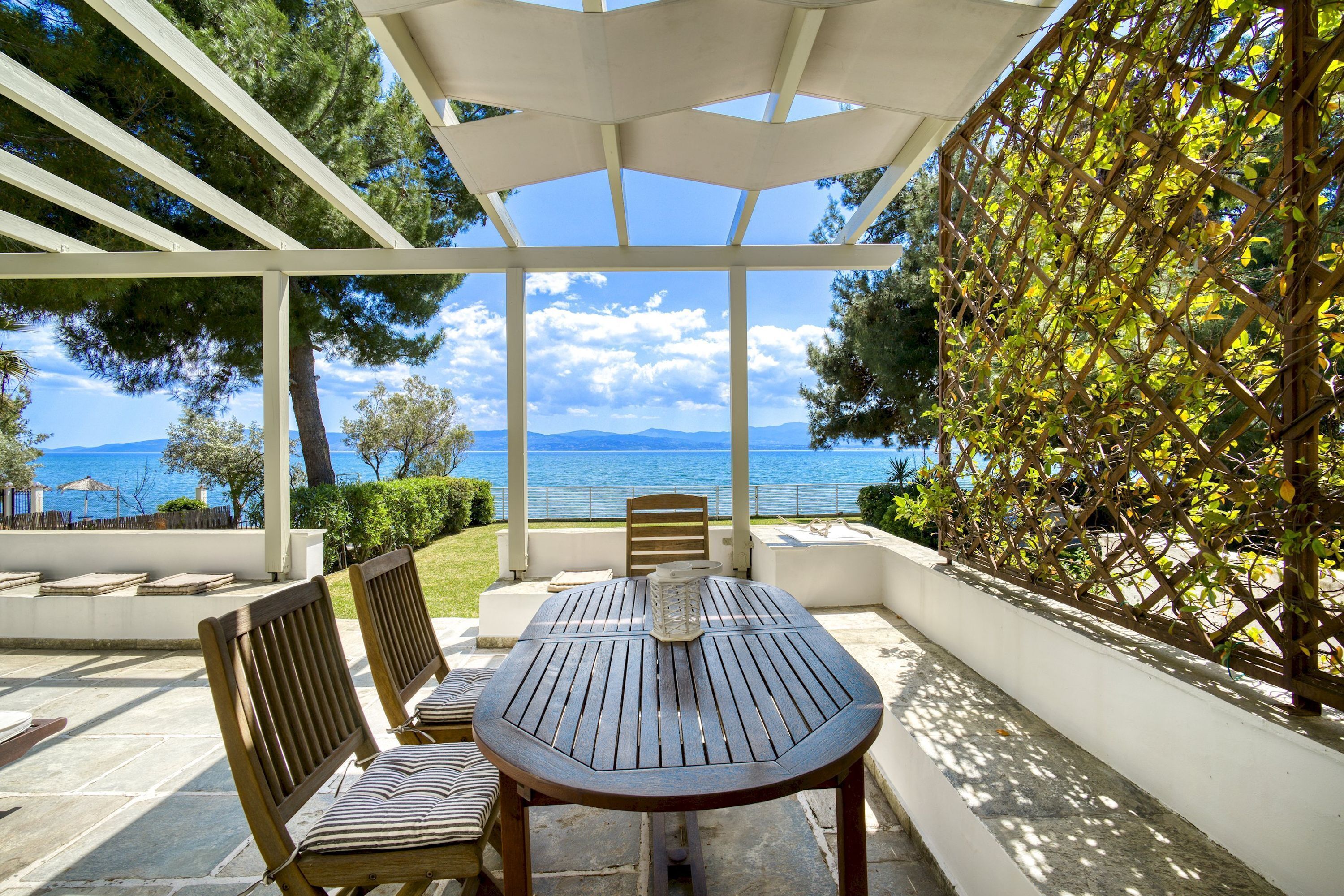 Un patio exterior con una mesa y sillas, una pérgola y vistas al mar y a las montañas.