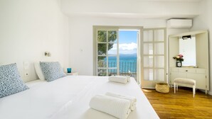 Un dormitorio con una cama grande, un banco, una mesita y vistas al mar.