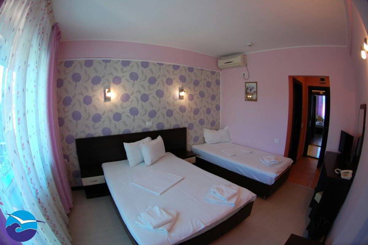 A hotel room with two beds, a headboard, a wall-mounted air conditioner, and a small desk with a telephone.