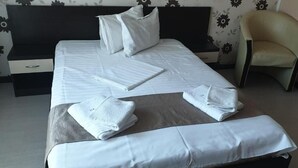 A neatly made bed with white linens, a chair, and a nightstand with a drawer. - Vila Alessia (Eforie)