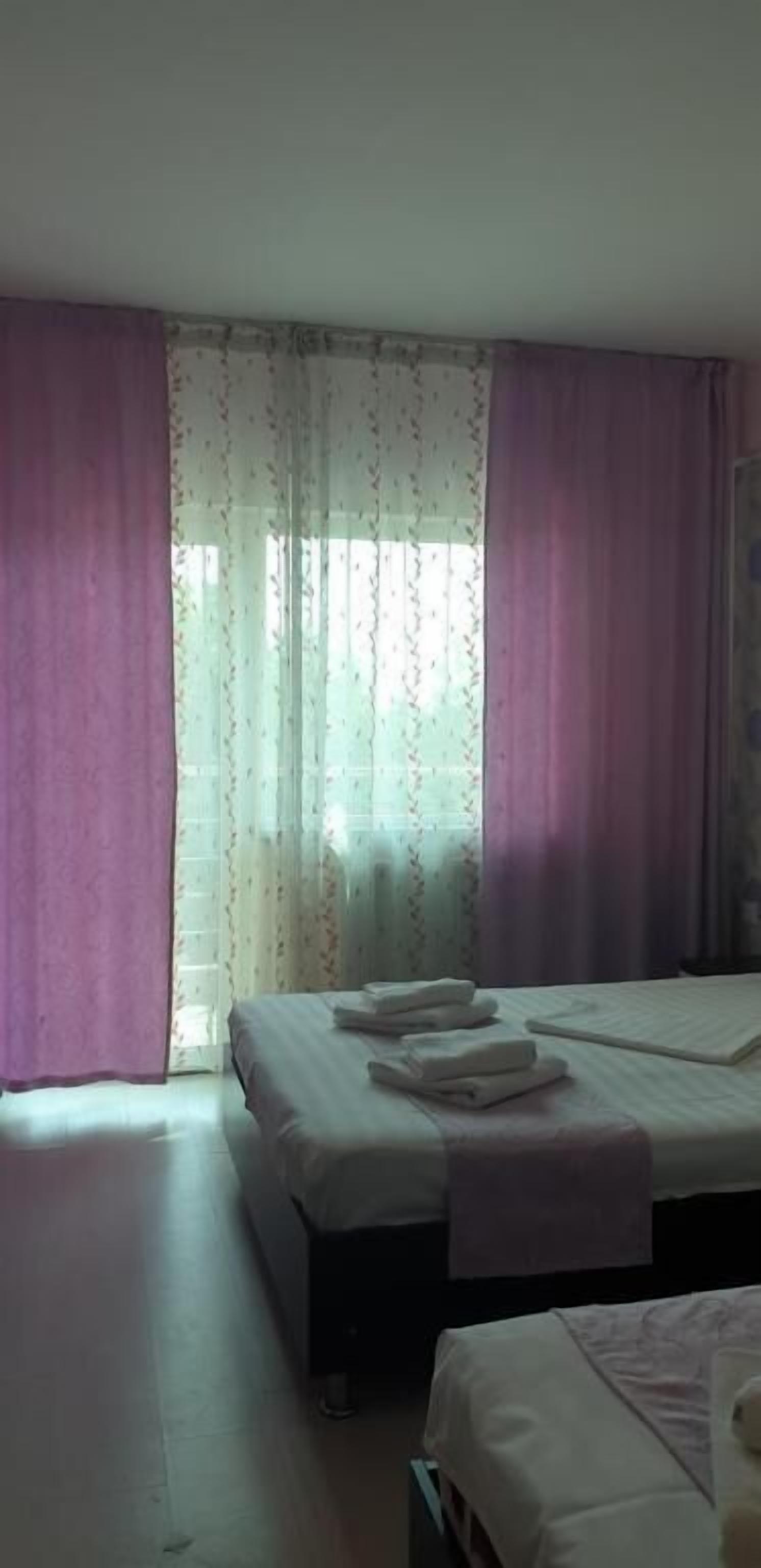 Een hotelkamer met twee bedden, een raam met dunne gordijnen en uitzicht op buiten.
