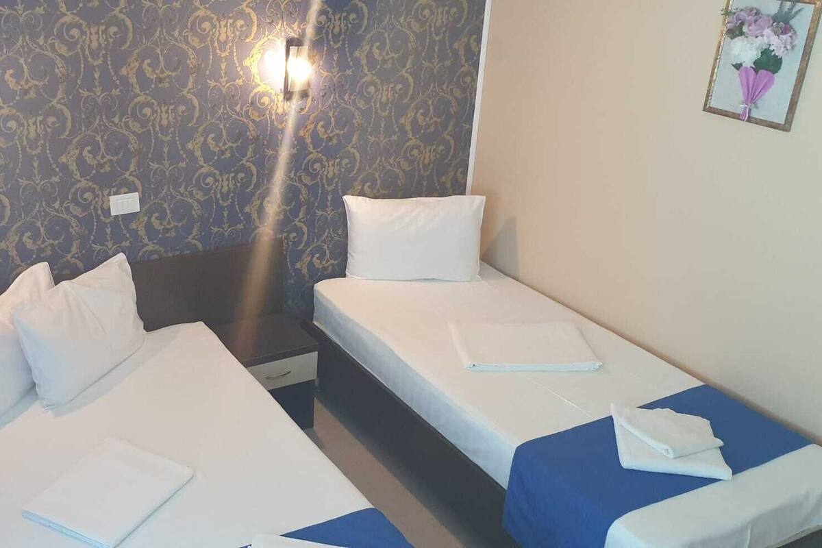A hotel room with two single beds, a nightstand, a small table, and a wall-mounted light fixture.