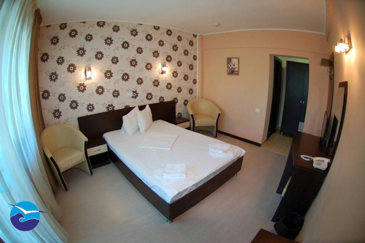 A hotel room with a large bed, two chairs, a desk with a telephone, and a mirror.