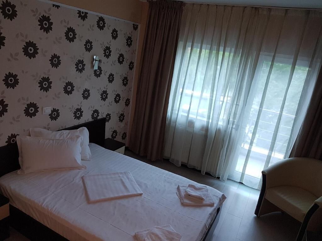 Une chambre d’hôtel avec un lit, une chaise et une fenêtre avec des rideaux.